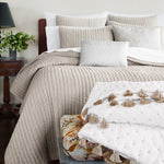 A bed with white cotton linen and John Robshaw embroidered Chandra Natural Kidney Pillows on it. - 30400087293998