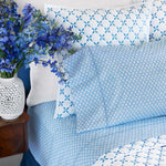 A bed with the John Robshaw Bindi Light Indigo Organic Sheet Set and a vase of organic percale flowers featuring a floral print. - 30395674624046