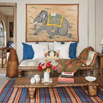 A Grey Elephant Running on Grass Tapestry from John Robshaw hangs on the wall of a colorful living room, evoking a sense of traveling. - 30720448823342