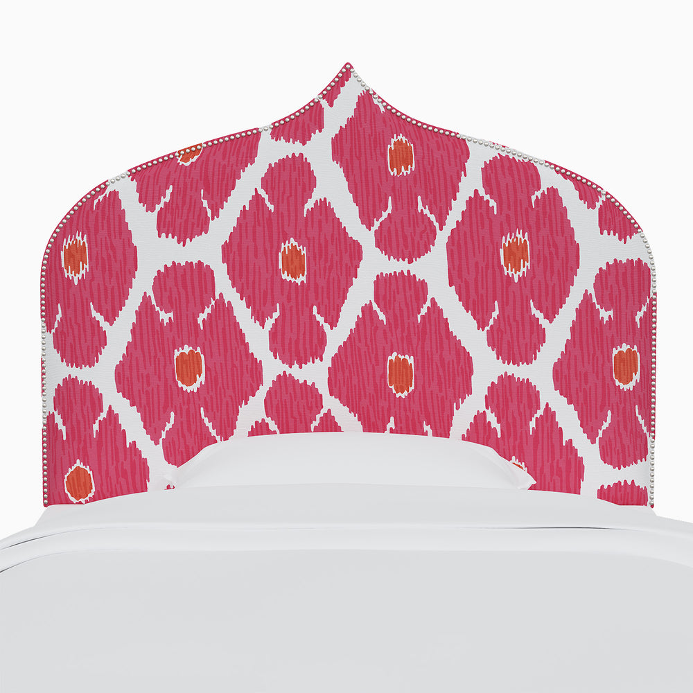 A bed with a pink and white John Robshaw Alina headboard featuring prints reminiscent of Mughal arches.