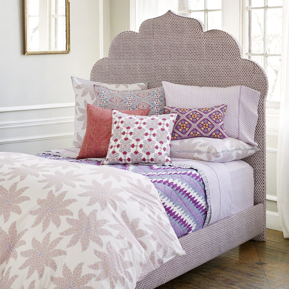 A John Robshaw Custom Bihar Bed adorned with vibrant purple and pink fabric bedding and pillows.
