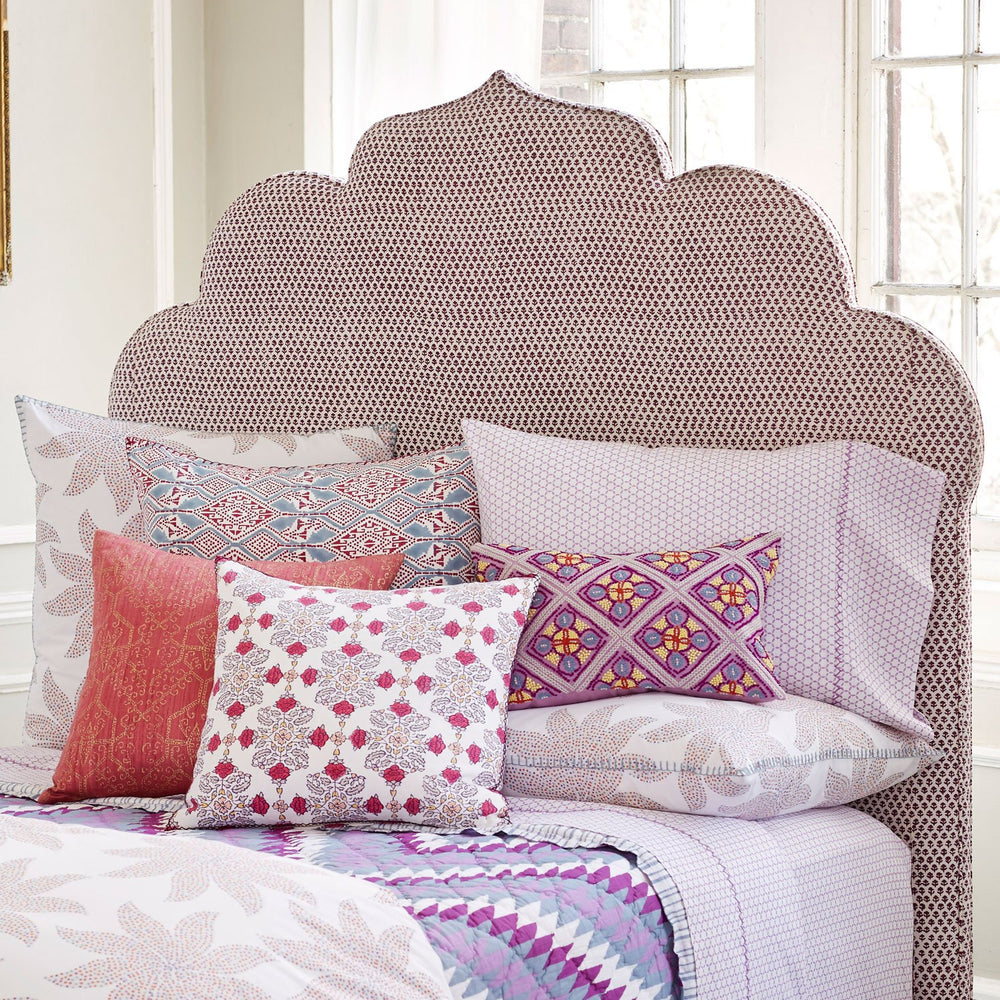 A handmade bed with white glove delivery, featuring purple and pink pillows and a Custom Bihar Headboard by John Robshaw.