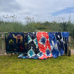 Four John Robshaw Sashpura Indigo Beach Towels hanging on a fence in front of a grassy area. - 29542059278382