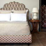 A bed with a patterned headboard covered in cotton chambray coverlets and adorned with hand stitching, featuring the Vivada Sand Woven Quilt by John Robshaw. - 30262782361646