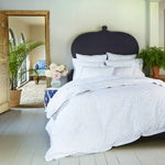 A bedroom with a bed and a bedside table, featuring the John Robshaw Vamika Periwinkle Organic Duvet. - 28783112290350