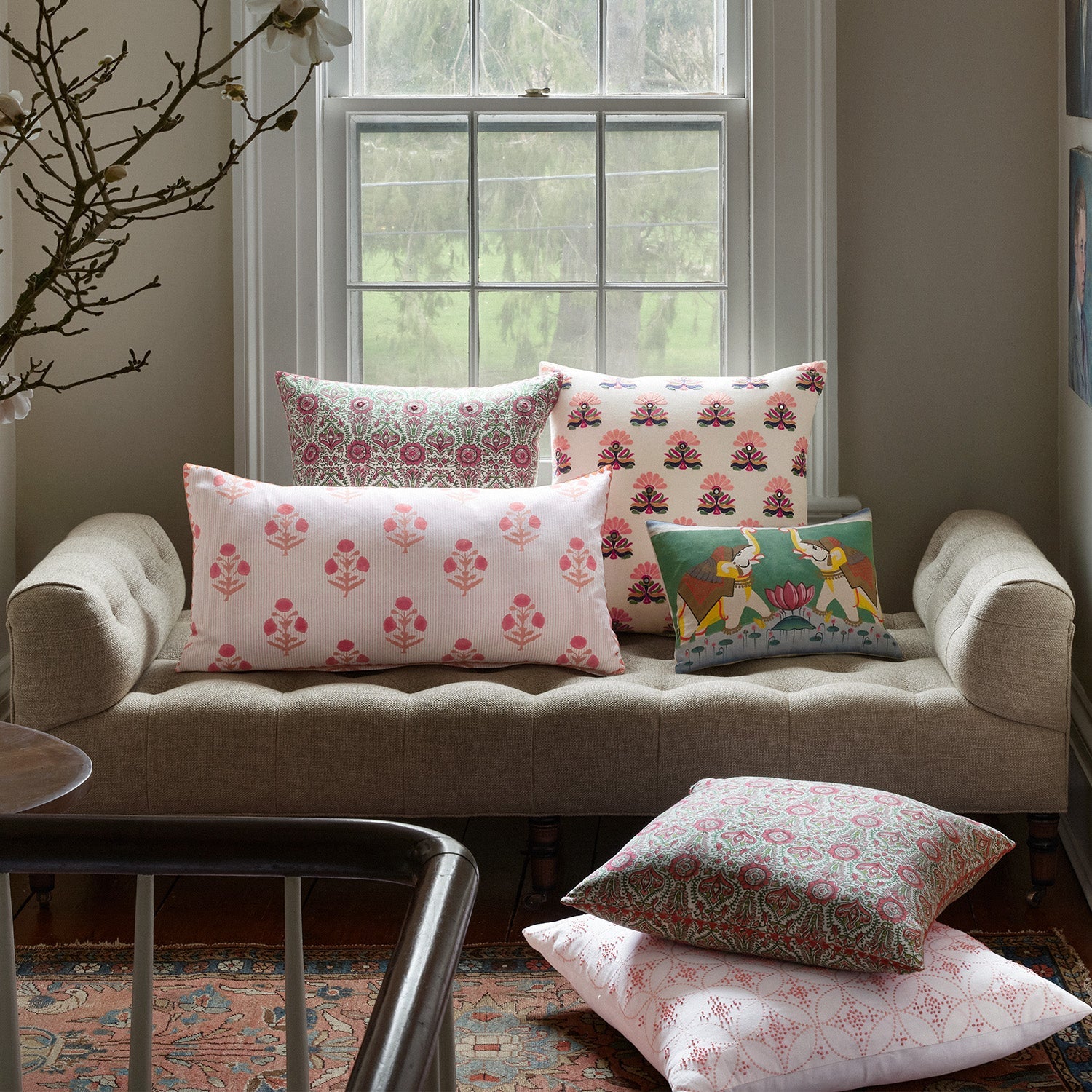 A collection of decorative pillows with floral and animal prints displayed on a gray tufted sofa in front of a window.