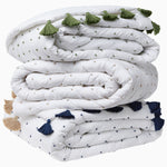 A stack of white and green French Knot Indigo Throw blankets with tassels and John Robshaw detailing. - 30497694908462