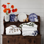 A wooden dresser adorned with French Knot Indigo Throw by Throws and a bouquet of flowers. - 30395702345774