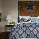 A bed with a Manav Decorative Pillow by John Robshaw and a hand printed blue and white comforter and a wall hanging. - 30403621519406