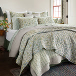 A bed with a Tiya Periwinkle Woven Quilt by Quilts & Coverlets featuring ornate vines. - 30395682652206
