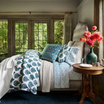 A bedroom with blue and white block printed bedding and hand stitched flowers, adorned with the Alagan Peacock Decorative Pillow by John Robshaw. - 30801408884782