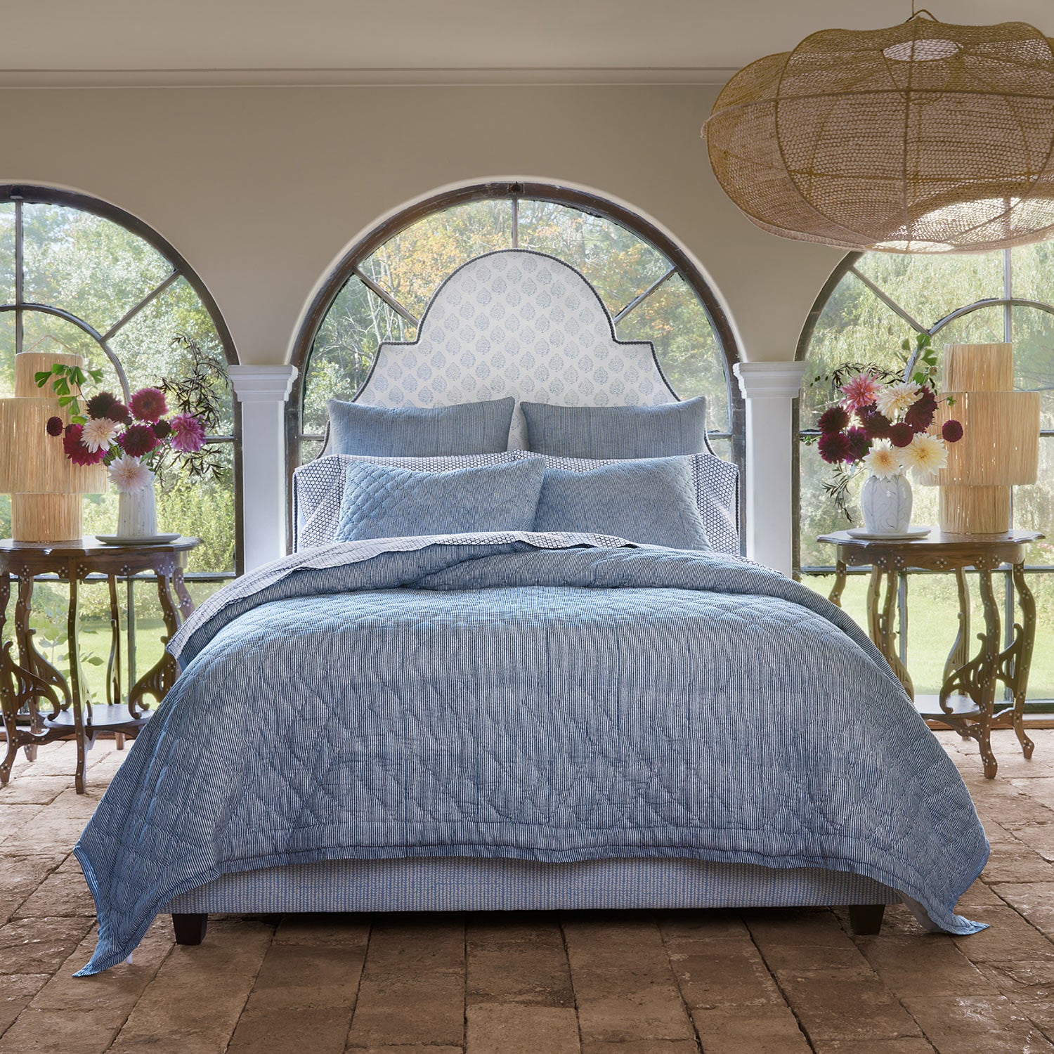 A bed with a simple Nandi Indigo Quilt by John Robshaw and arched windows.