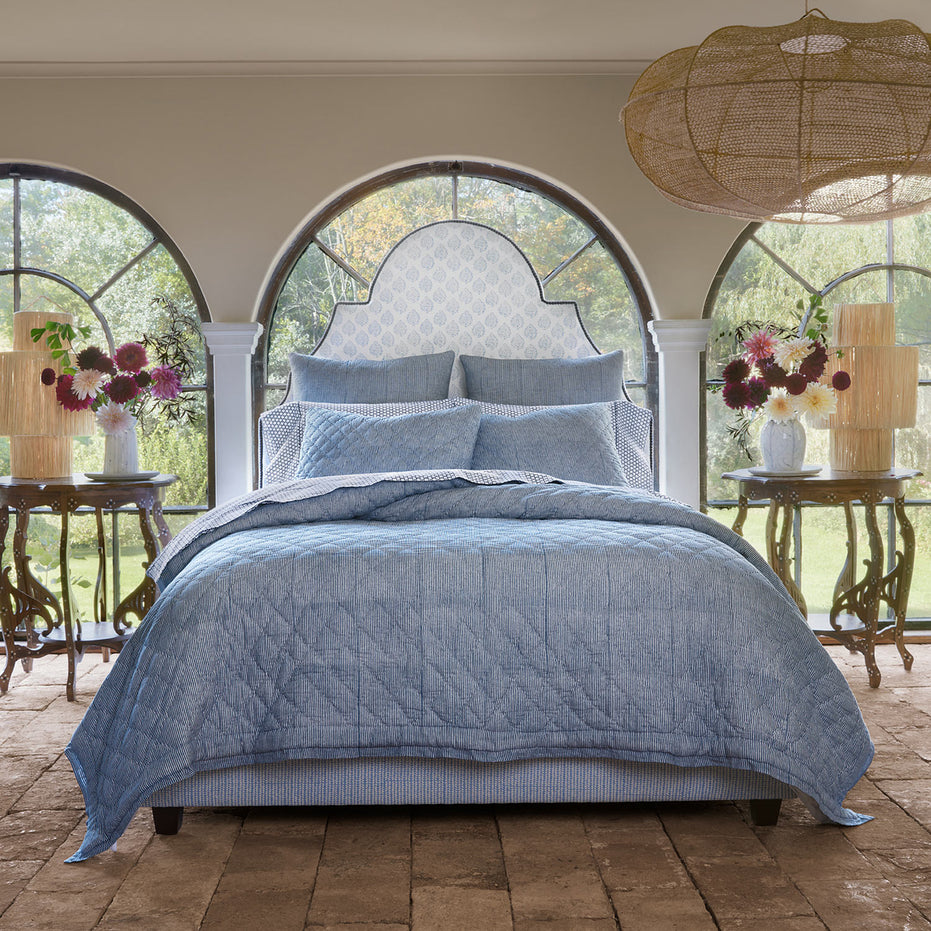 A bed with a simple Nandi Indigo Quilt by John Robshaw and arched windows.