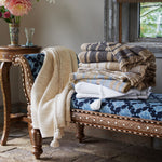 A stack of John Robshaw Ekram Indigo Throw blankets on a bench in front of a window. - 30784359465006