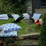 An Aleesa Light Indigo Outdoor Decorative Pillow stacked on top of a stone wall. - 30801471242286
