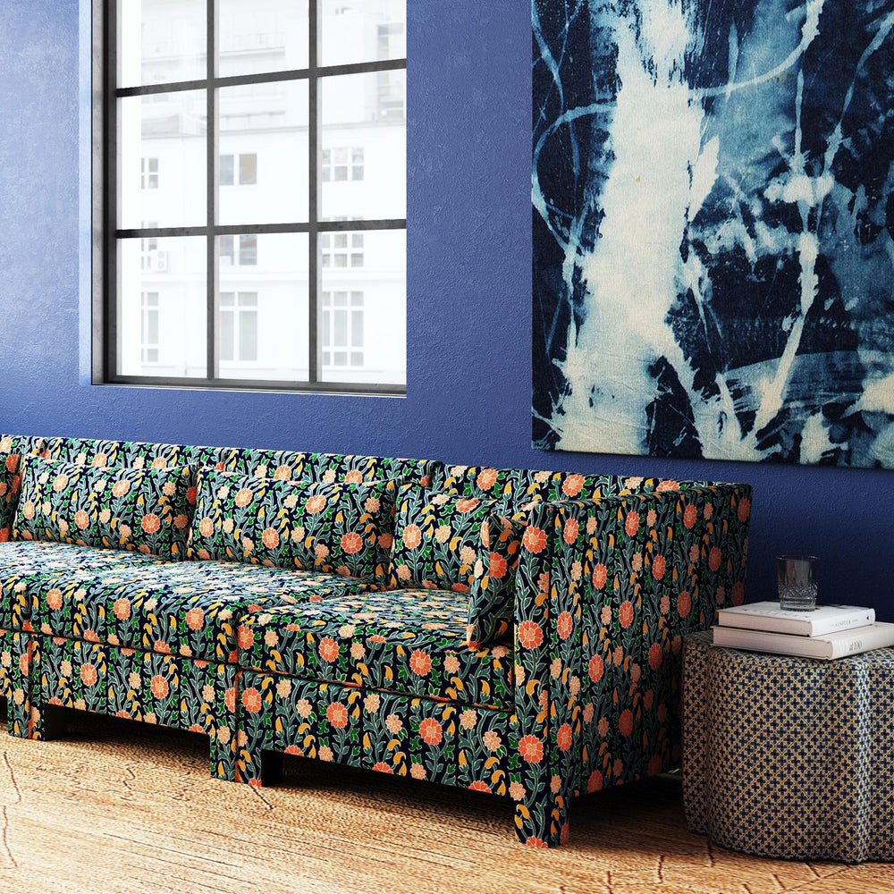 A couch with a Shiza Ottoman by Skyline in a living room with a painting of John Robshaw's Kashmir gardens on the wall.