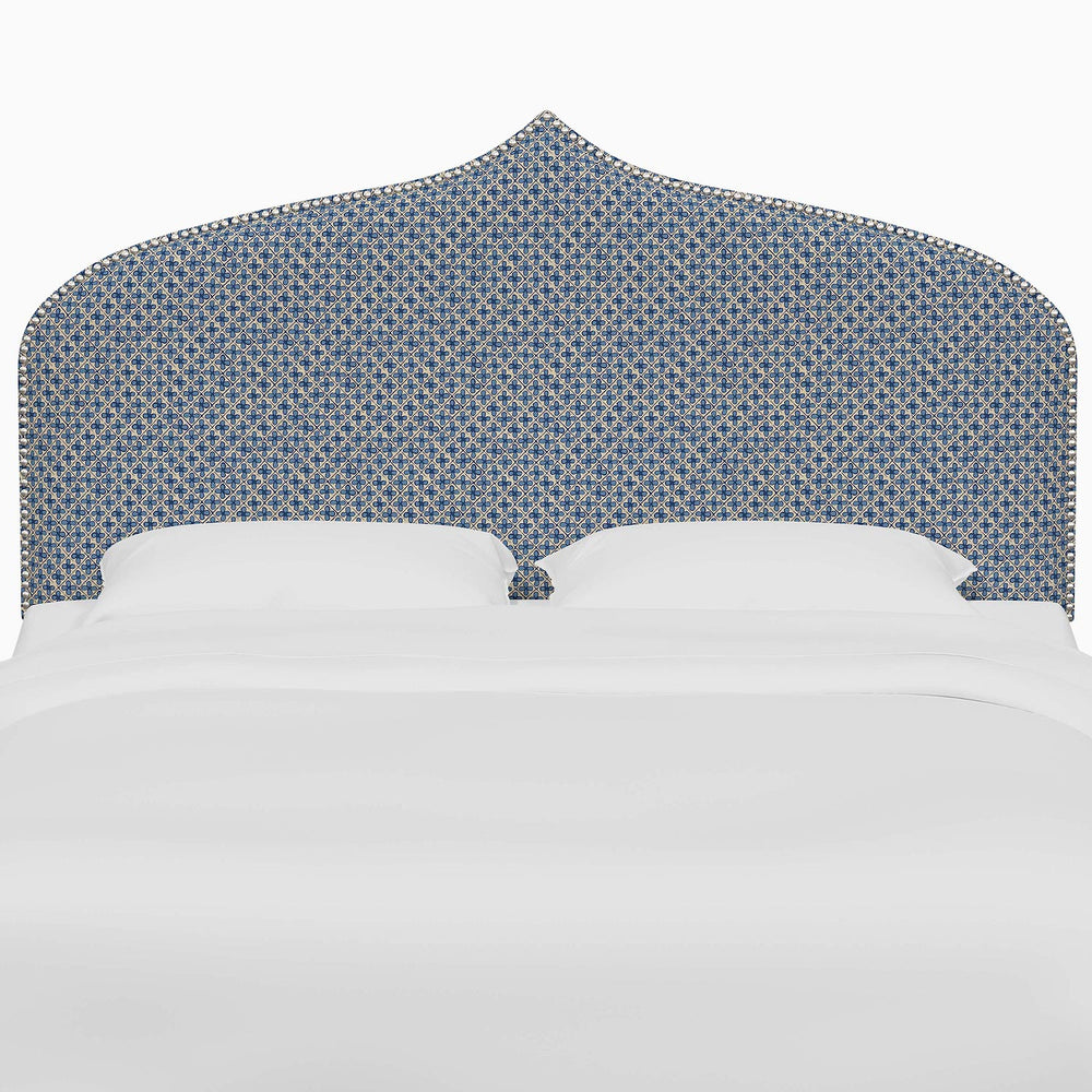 A bed with a blue John Robshaw Alina headboard and white sheets featuring Mughal arches prints.