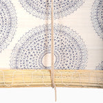 A close-up of John Robshaw Textiles' Lapis Chik Blinds features intricate blue circular patterns and hangs above a handmade bamboo blind, with a vertical rope down the center. - 31884733481006