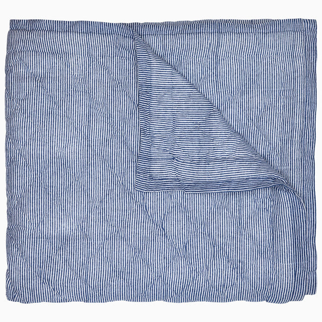 A Nandi Indigo Quilt by John Robshaw, hand quilted and featuring blue stripes, folded on top of itself.