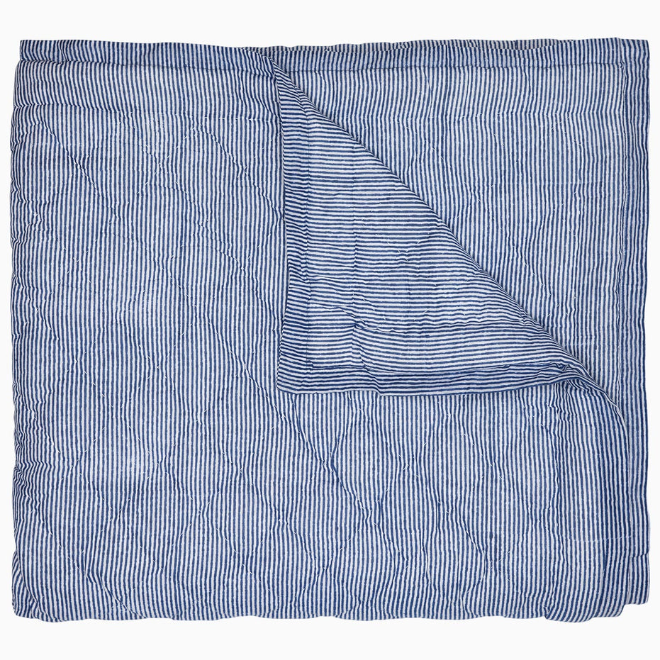 A Nandi Indigo Quilt by John Robshaw, hand quilted and featuring blue stripes, folded on top of itself.