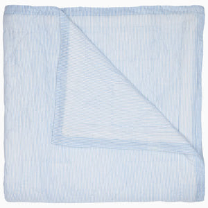 A Nandi Light Indigo quilt by John Robshaw with blue and white striped block printing on a white background.