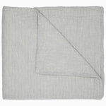 A reversible Vivada Light Gray Woven Quilt with hand stitching designs, folded neatly on top of a white cotton chambray surface. (Brand Name: John Robshaw) - 30776292704302