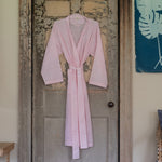 A unisex pink Kahini Robe, made of cotton voile, hangs on a wooden door. (John Robshaw) - 30822536577070