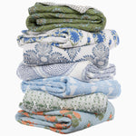 A stack of six John Robshaw Jeeva Sage Quilts, each beautifully hand quilted with a variety of floral patterns and colors such as blue, green, and orange, arranged in a vertical pile. These soft cotton quilts feature intricate spring meadow designs that add a touch of nature to any room. - 31274123853870