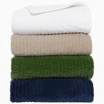 Stack of five neatly folded Velvet White Quilts by John Robshaw, featuring hand-quilted cotton velvet in white, beige, green, and blue shades against a white background. - 31274123460654