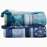 Two stacked, folded John Robshaw Malvika Peacock Throws with tassels: the bottom one in blue featuring white and teal patterns, and the top one in teal adorned with white and light blue patterns. Both throws are crafted from soft cotton voile and showcase exquisite hand-printed designs. - 31274109009966