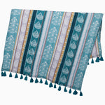 The Malvika Peacock Throw by John Robshaw is a beautifully patterned textile with vertical teal, white, and yellow stripes, adorned with intricate paisley and floral designs. It features teal tassels along the bottom edge and is crafted from hand-printed cotton voile for a distinctive touch. - 31272464744494