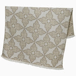 A John Robshaw Dasati Sand Throw, featuring a beige fabric with an intricate leaf-like woven design and fringed edging, draped open against a plain background. - 31272471494702