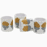 The Nand Metallic Beaded Napkin Rings (Set of 4) by Tabletop feature exquisite gold and silver floral patterns on a white backdrop, creating an elegant embrace that adds a touch of sophistication to any dining setting. - 31272678981678