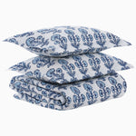 A folded Ojas Indigo Organic Duvet from John Robshaw, made of white cotton percale, with two pillows featuring a blue floral block print pattern stacked on top. - 31272409727022