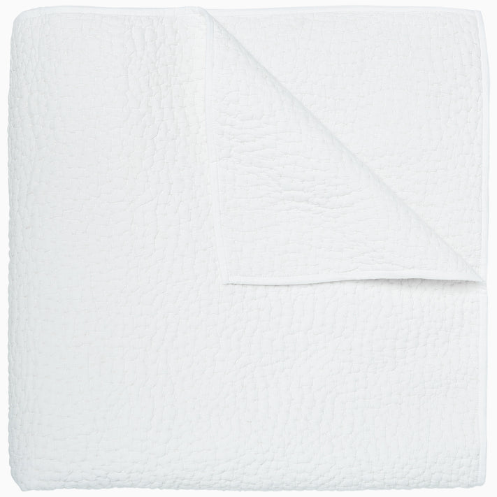 An Organic Hand Stitched White Quilt by John Robshaw folded on top of a white surface.