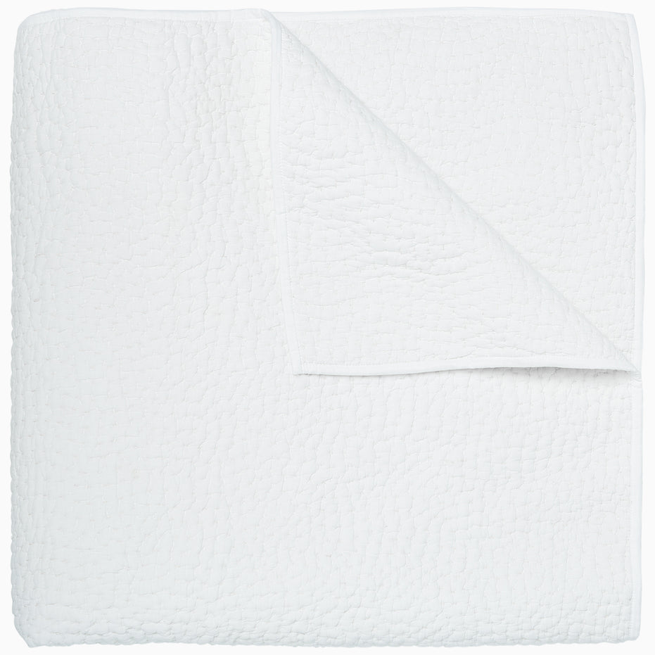 An Organic Hand Stitched White Quilt by John Robshaw folded on top of a white surface.