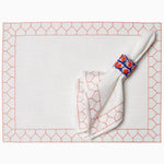 A Set of 4 John Robshaw Stitched Coral Napkins, made of 100% cotton slub, machine washable and hand stitched, neatly resides in a sleek napkin holder on a white table. - 29333296381998