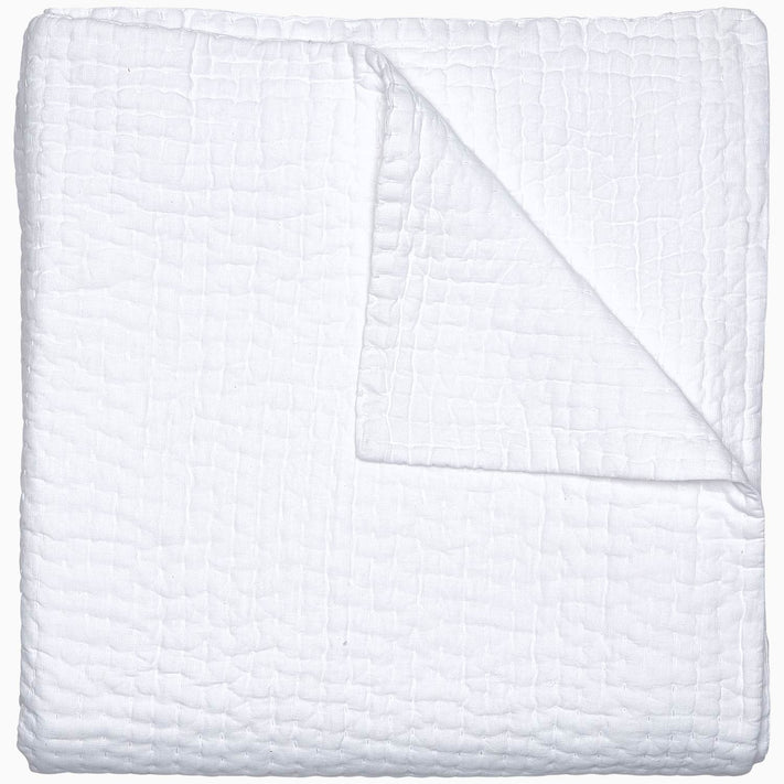 A Vivada White Woven Quilt by John Robshaw folded on top of a white surface with hand stitching.