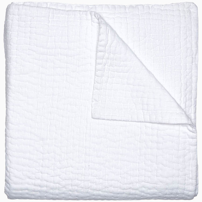 A Vivada White Woven Quilt by John Robshaw folded on top of a white surface with hand stitching.
