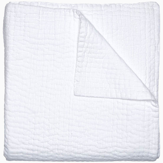 A Vivada White Woven Quilt by John Robshaw folded on top of a white surface with hand stitching.