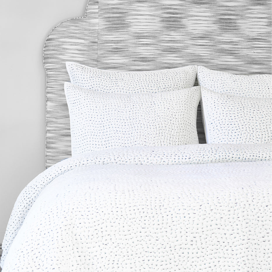 A cotton voile bed cover with a blue and white polka dot duvet cover, featuring the Organic Hand Stitched Light Indigo Quilt by John Robshaw.