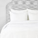A John Robshaw Organic Hand Stitched White Quilt with organic cotton pillows and a hand-stitched headboard.