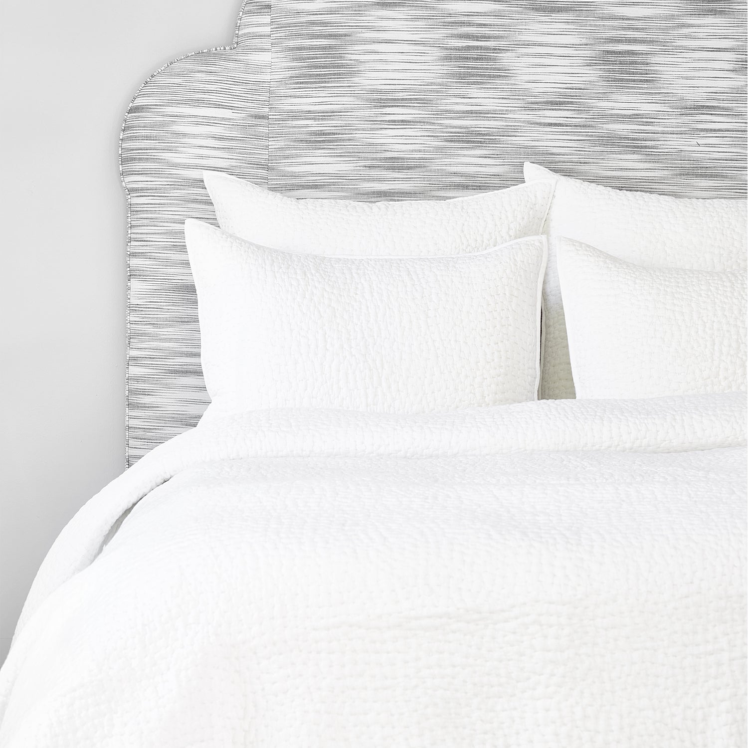 A John Robshaw Organic Hand Stitched White Quilt with organic cotton pillows and a hand-stitched headboard.