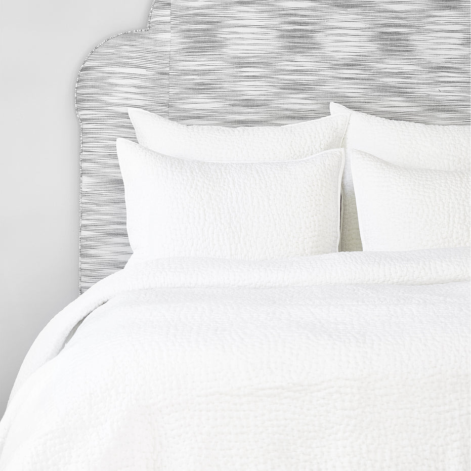 A John Robshaw Organic Hand Stitched White Quilt with organic cotton pillows and a hand-stitched headboard.