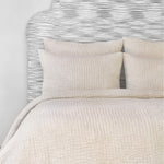 A bed with a beige headboard and white pillows adorned with John Robshaw cotton chambray coverlets. - 28271561867310