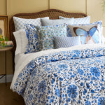 A bed with embroidered designs on a blue and white floral comforter made of stitched indigo organic sheets by John Robshaw. - 30270347706414