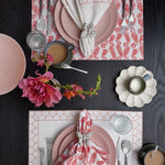 A table setting with pink and white printed plates and silverware, complemented by John Robshaw's Aamani Coral Napkins (Set of 4). - 30009671417902