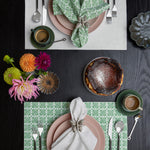 A table setting with Pavati Sage Napkins (Set of 4) by John Robshaw in springlike colors on a black table. - 30009670959150