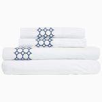 A stack of Sana Indigo Organic Sheet Sets by Sheets & Cases with a hand-embroidered chain motif. - 28739470786606