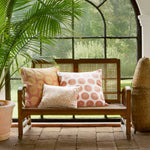 A John Robshaw wooden and cane sofa - 3 seat with pillows in front of a window. - 29553973329966